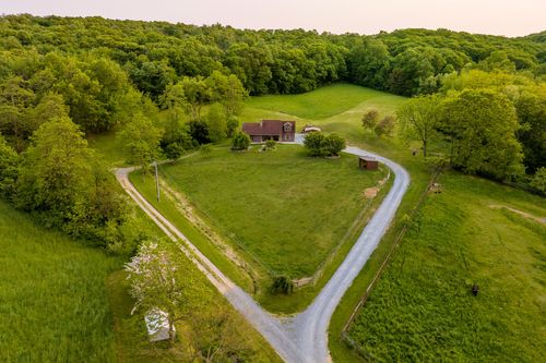 Aerial view of a brick farmhouse with a covered porch and gravel driveway