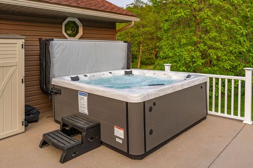 Hot tub on a covered patio beside wood siding and an octagon window