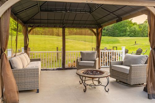 Gazebo lounge with a wicker sofa, armchairs and a fire pit table overlooking green lawn