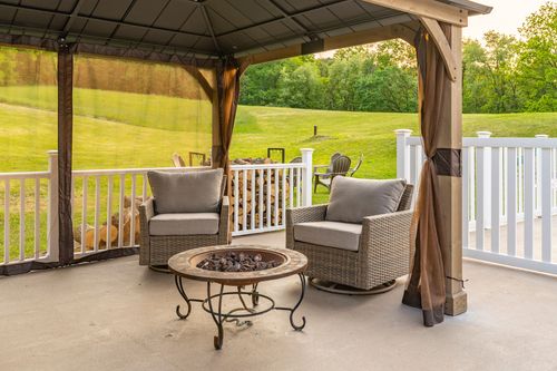 Covered gazebo seating area with wicker chairs and a stacked firewood rack