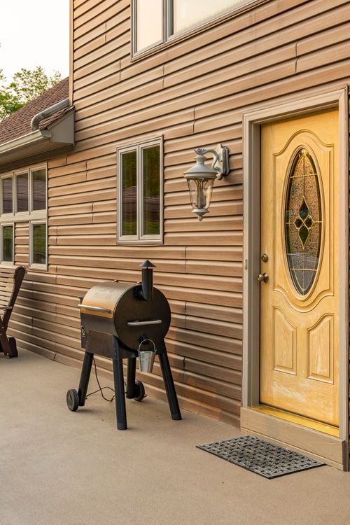 Wood-sided farmhouse exterior with a yellow front door and outdoor smoker grill