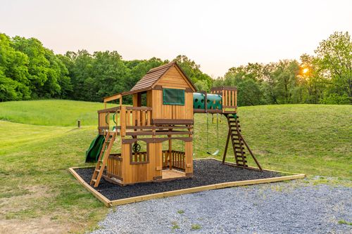 Two-story wooden play set with a slide and climbing wall on a mulch bed