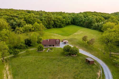 Aerial view of a red brick farmhouse with a covered porch and patio at dusk
