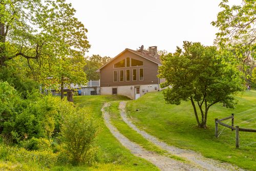 Exterior of a brown farmhouse viewed from a curving gravel driveway at dusk