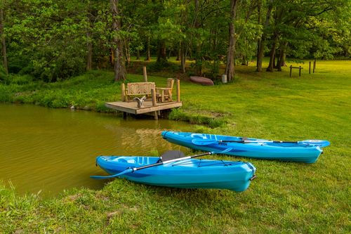Two blue kayaks with paddles on the lawn beside a pond and wooden dock