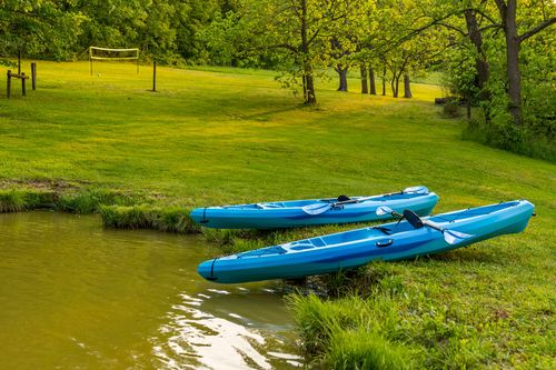 Two blue kayaks on the grassy bank of a pond near a volleyball net