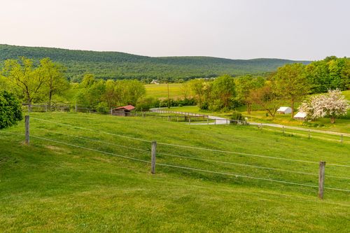 Fenced pasture with a small pond and red-roofed barn beneath distant mountains