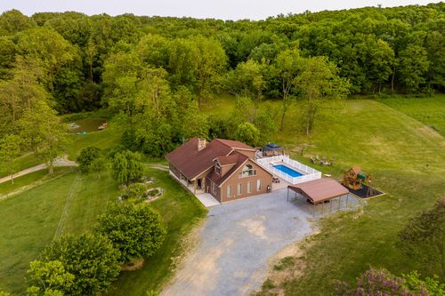 Aerial view of a farmhouse with a pool and playground set against distant mountain ridges