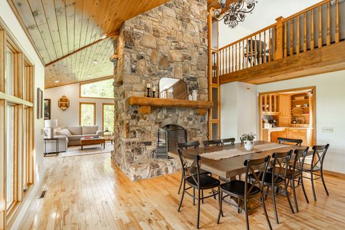Great room with a floor-to-ceiling stone fireplace, wood dining table and open loft