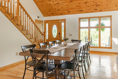 Dining room with a farmhouse table, wood staircase and large windows to a deck