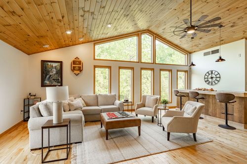 Open living room with a vaulted wood ceiling, ceiling fan and a kitchen bar beyond