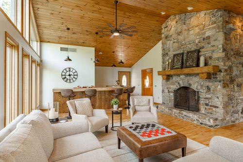 Living room with a stone fireplace and checkerboard ottoman beside a kitchen bar