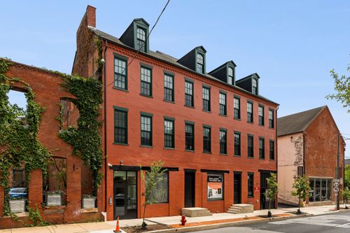 Street view of a restored brick building with dormer windows next to an ivy-draped ruin wall