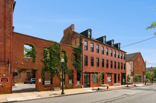 Historic brick facade with arched window openings overtaken by climbing ivy along the sidewalk