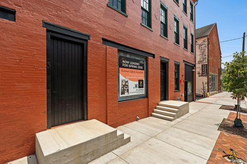 Brick building entrance with a black paneled door, stone steps and a now-leasing sign