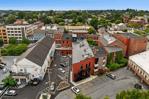 Aerial view of a brick loft complex with rooftop patio seating above a parking area