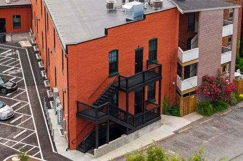 Aerial view of a red brick building's rear facade with black fire escapes and a parking lot