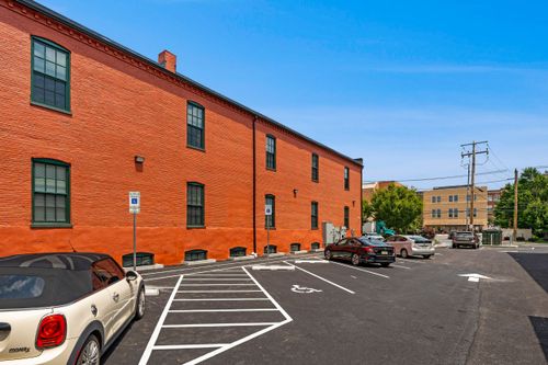 Brick apartment building exterior with green-trimmed windows and a rear parking area