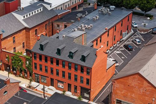 Aerial view of a red brick building with rooftop patio seating and a slate mansard roof
