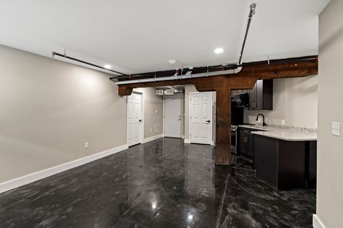 Open loft living area with polished black floors, dark cabinetry and an exposed wood ceiling beam