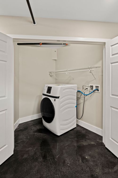 Laundry closet with a white front-load washer, wire shelving and dark polished flooring