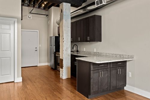 Loft kitchen with dark cabinets, granite counters, exposed ceiling joists and hardwood flooring