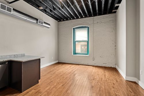 Open loft room with exposed ceiling joists, a whitewashed brick wall and teal-trimmed window