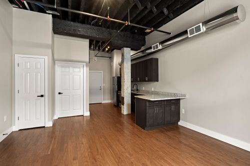 Open loft living area with hardwood floors, white paneled doors and a compact kitchenette