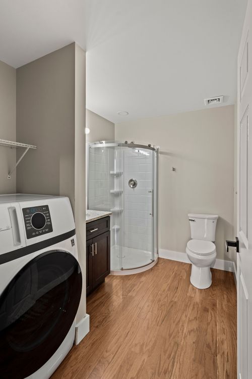 Bathroom with a curved glass shower, toilet and a front-load washer tucked in the corner