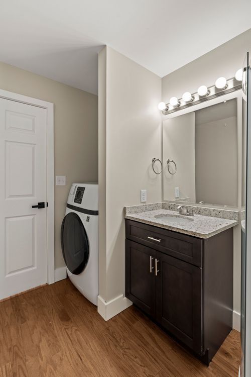 Bathroom vanity with a mirrored light fixture beside a stacked washer and dryer