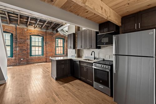 Loft kitchen framed by exposed brick walls, teal-trimmed windows and a natural wood ceiling