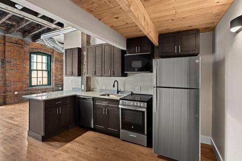Kitchen with a wood-plank ceiling, dark cabinetry, stainless appliances and exposed brick wall