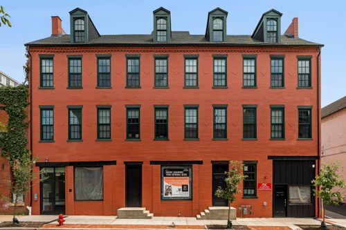 Four-story red brick apartment building with dormer windows and ground-floor commercial entrances