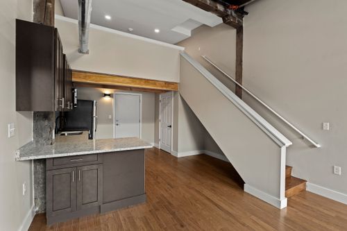 Open loft with a dark cabinet kitchen, wood beam ceiling and a staircase with white risers
