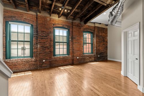 Loft living space with exposed brick, three arched teal-trimmed windows and a wood beam ceiling