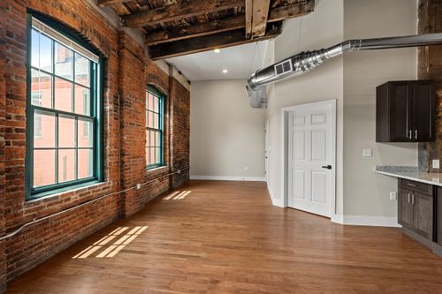 Open loft room with exposed brick, teal-trimmed windows and reclaimed wood ceiling beams