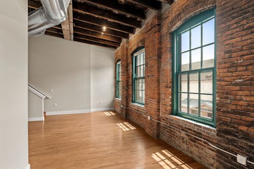 Sunlit loft room with exposed brick walls, arched teal windows and open wood ceiling joists