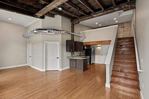 Loft living area with a wood staircase, small kitchenette and exposed overhead ductwork