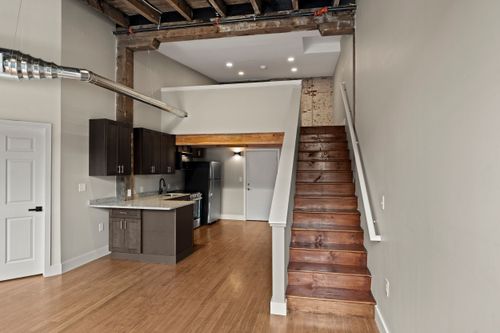 Loft kitchen with dark cabinets beside a wood staircase and exposed ceiling beams