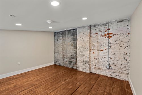 Empty loft room with a weathered whitewashed brick accent wall and dark hardwood floors