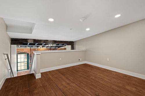 Open loft landing with a half wall railing overlooking a brick window and wood floors