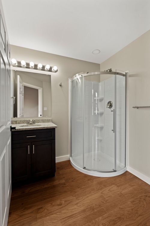 Bathroom with a subway-tiled corner shower, dark vanity and warm wood-look flooring