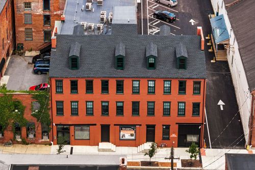 Aerial view of a brick building with copper-topped dormers beside a paved parking lot