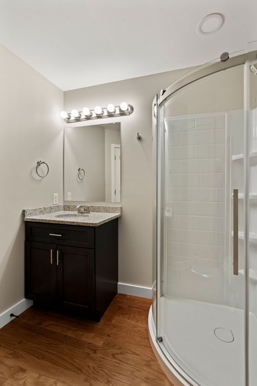 Bathroom with a dark wood vanity, granite counter and a curved glass shower enclosure