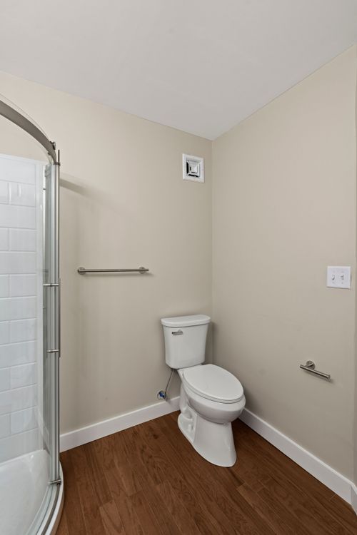 Bathroom with a white toilet, towel bars and a corner glass shower on wood-look flooring