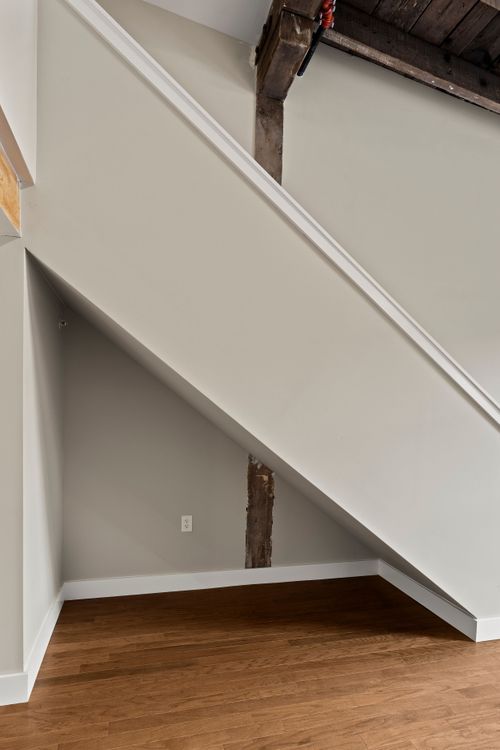 Under-stair storage nook with white paneled walls and a rustic wood ceiling beam above