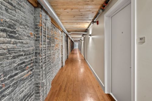 Corridor with an exposed stone and brick wall leading past numbered apartment doors