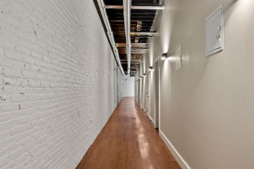 Long interior corridor with a whitewashed brick wall, wall sconces and apartment doors