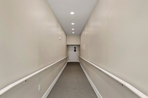 Long interior hallway with wall-mounted handrails leading to a keypad-secured door