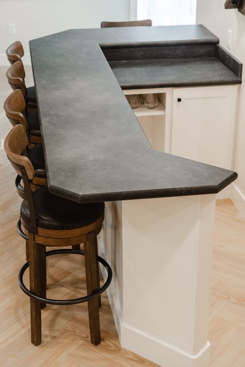 Basement wet bar with a soapstone counter, herringbone flooring and leather-seat barstools